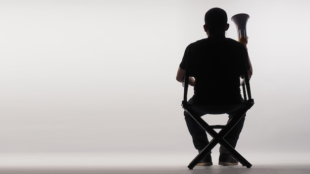 Sulla schiena di un uomo asiatico seduto sulla sedia nera del regista con un megafono su sfondo bianco