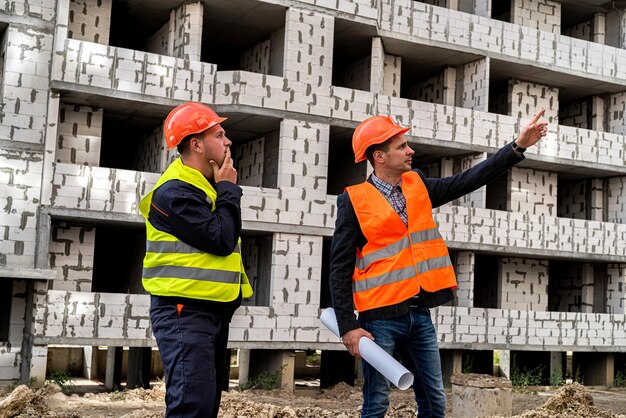 Sullo sfondo dell'edificio in costruzione due giovani lavoratori in tuta stanno con le spalle guardando il nuovo concetto di costruzione di edifici