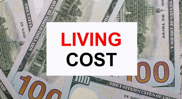 Sullo sfondo di dollari americani, una carta bianca con il testo LIVING COST. Concetto finanziario