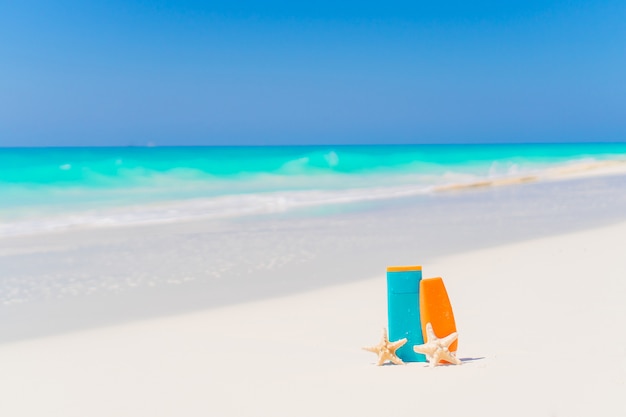 Suncream bottiglie, bicchieri, stelle marine sulla spiaggia di sabbia bianca