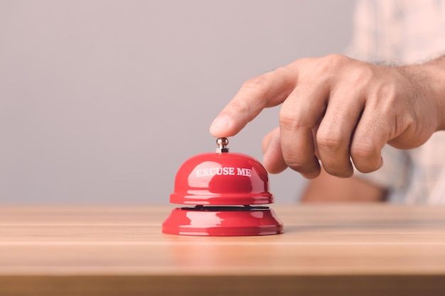 Suonare a mano il campanello rosso o il campanello di servizio sulla scrivania in legno marrone con sfondo grigio per il concetto di pubblicità di hotel o ristoranti