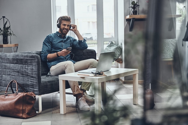 Suono incredibile. Bel giovane uomo moderno che ascolta musica mentre è seduto al suo posto di lavoro