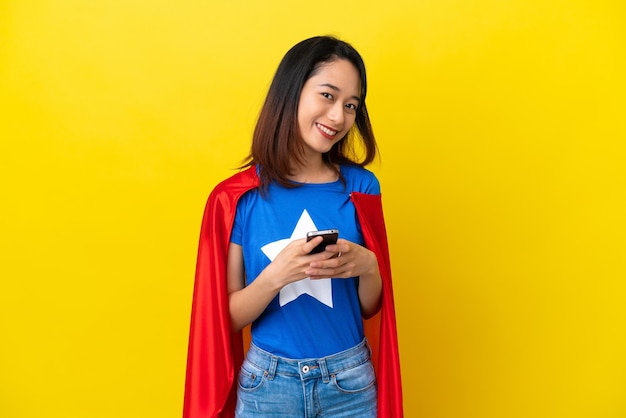 Super eroe donna vietnamita isolata su sfondo giallo che invia un messaggio con il cellulare