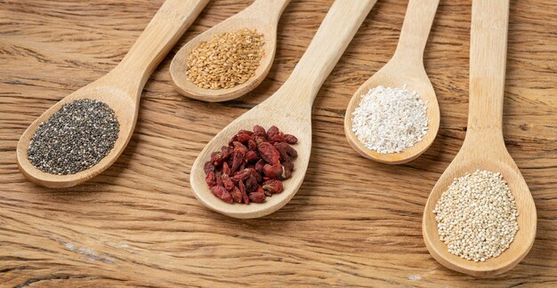 Supercibi assortiti in cucchiai sul tavolo di legno. Chia, quinoa, avena, semi di lino e bacche di goji.