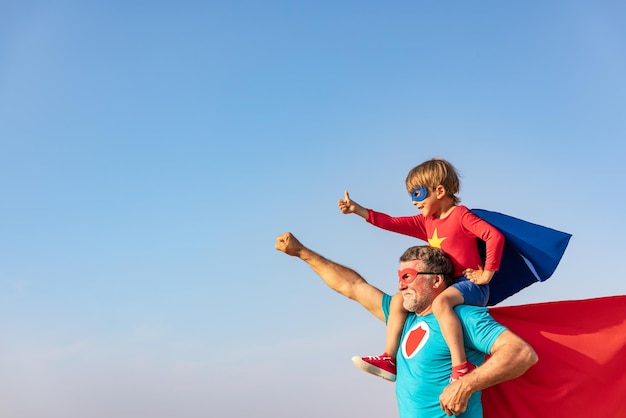 Supereroe uomo anziano e bambino che giocano all'aperto. Super eroe nonno e ragazzo che si divertono insieme. Concetto di vacanza in famiglia. Buona festa del papà