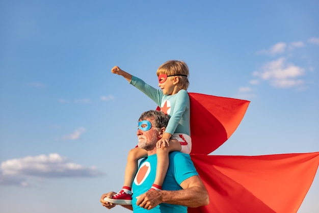 Supereroe uomo anziano e bambino che giocano all'aperto. Super eroe nonno e ragazzo che si divertono insieme sullo sfondo blu del cielo estivo. Concetto di vacanza in famiglia. Buona festa del papà