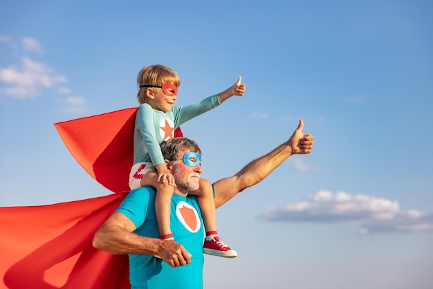 Supereroe uomo anziano e bambino che giocano all'aperto Super eroe nonno e ragazzo che si divertono insieme sullo sfondo blu del cielo estivo Concetto di vacanza in famiglia Felice festa del papà