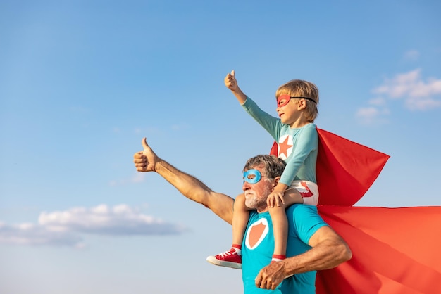 Supereroe uomo anziano e bambino che giocano all'aperto Super eroe nonno e ragazzo che si divertono insieme sullo sfondo blu del cielo estivo Concetto di vacanza in famiglia Felice festa del papà