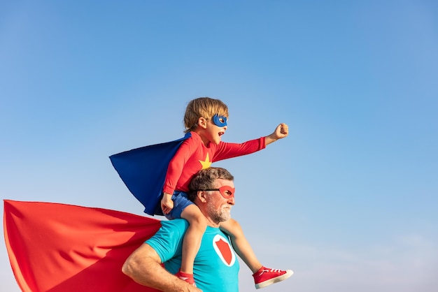 Supereroe uomo anziano e bambino che giocano all'aperto Super eroe nonno e ragazzo che si divertono insieme sullo sfondo blu del cielo estivo Concetto di vacanza in famiglia Felice festa del papà