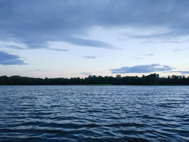 Superficie calma del lago alla sera in Lettonia, Europa orientale. paesaggio al tramonto estivo con acqua e foresta.