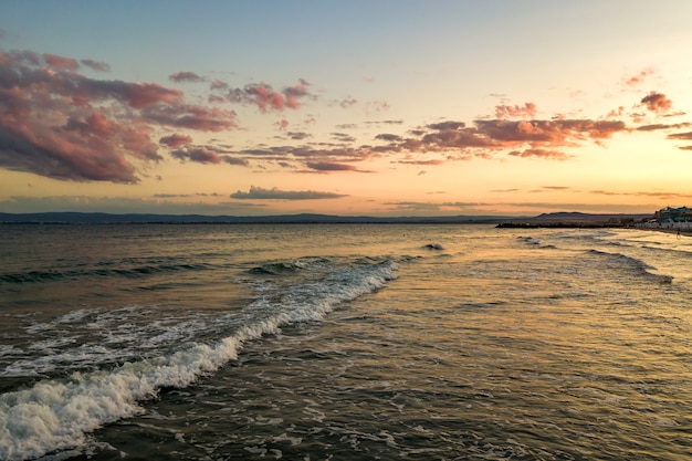 Superficie del mare con onde di acqua blu sotto il cielo al tramonto giallo e viola.