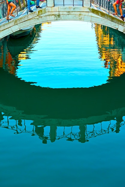 Superficie dell'acqua del canale veneziano con reflazione di un ponte con persone che camminano, Venezia, Italy