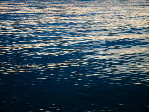 Superficie dell'acqua di mare blu scuro con riflessi di luce solare fioca