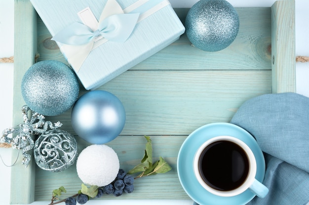 Superficie natalizia con una confezione regalo, una tazza di palline di caffè e un ramo con bacche su un morbido vassoio blu