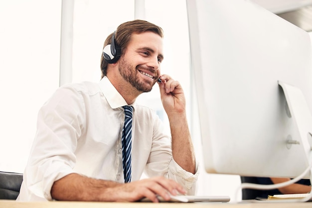 Supporto online del call center e uomo nel telemarketing con il sorriso mentre si consulta ascoltando e leggendo la posta elettronica sul computer Comunicazione Crm e addetto al servizio clienti nel supporto tecnico con il pc