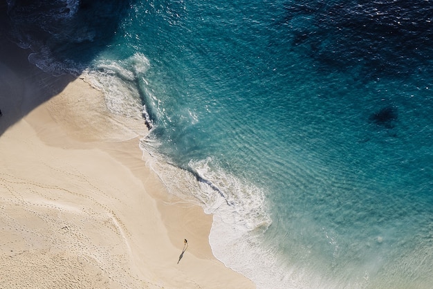 Surf di acqua blu della spiaggia sabbiosa e una persona cammina sulla spiaggia