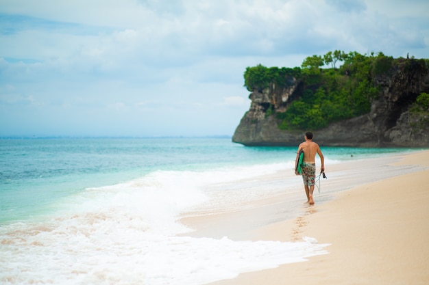 Surfer. Uomo di surf con la tavola da surf che cammina sulla spiaggia tropicale di sabbia.