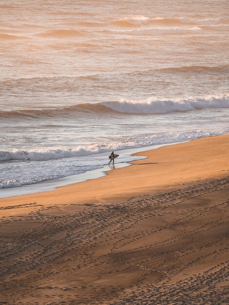 Surfista che corre per l'orlo della spiaggia di Nazaré