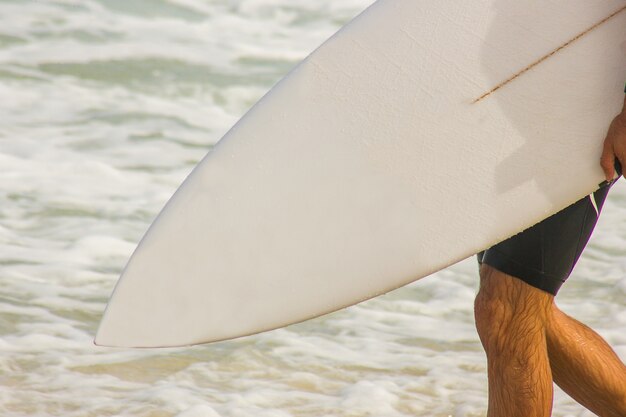 Surfista con tavola da surf che va verso il mare sulla spiaggia di Barra da Tijuca a Rio de Janeiro.