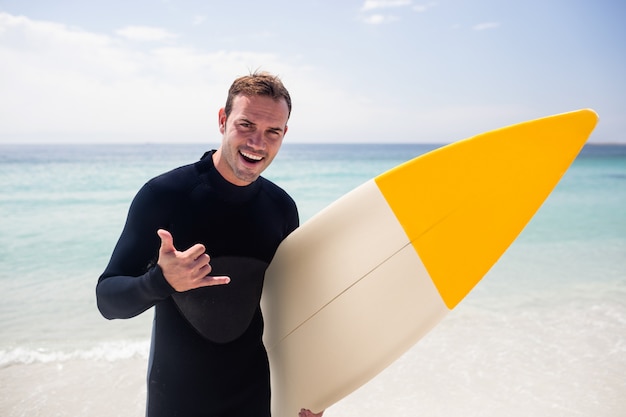 Surfista con tavola da surf gesticolano segno della mano sulla spiaggia