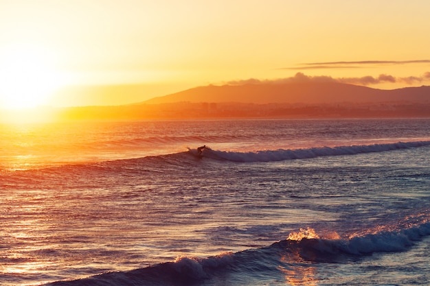 Surfista con tavola da surf sulle onde dell'Oceano Atlantico sulla spiaggia al tramonto, Portogallo