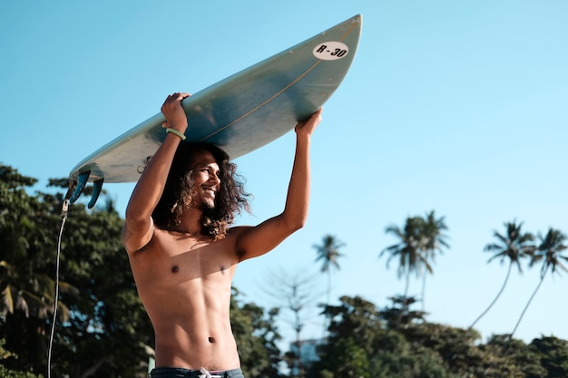 Surfista dell'uomo che si siede alla tavola da surf sulla spiaggia di sabbia