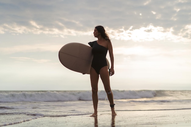 Surfista della donna con la tavola da surf sull'oceano al tramonto