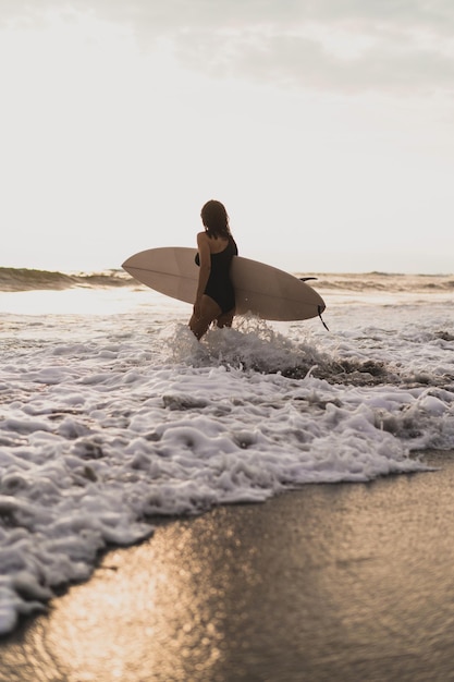 Surfista della donna con la tavola da surf sull'oceano al tramonto