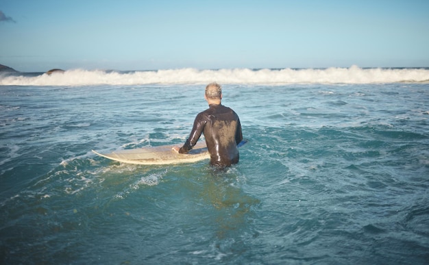 Surfista e uomo in acqua che guardano l'onda per l'alta marea mentre si tiene la tavola da surf sulla soleggiata spiaggia degli Stati Uniti