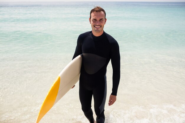 Surfista felice che tiene una tavola da surf sulla spiaggia