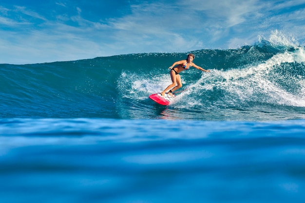 Surfista femminile su un'onda blu al giorno pieno di sole