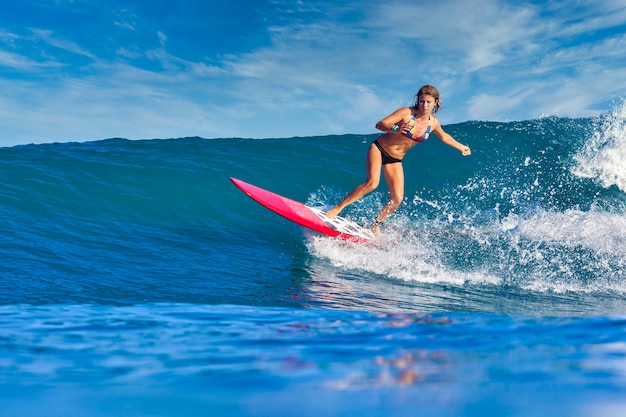 Surfista femminile su un'onda blu al giorno pieno di sole