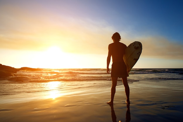 Surfista guardando il tramonto sulla spiaggia