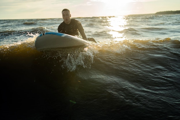Surfista maschio in una muta sulle onde al tramonto nel mare