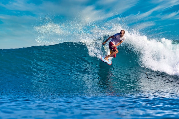 Surfista maschio su un'onda blu al giorno pieno di sole