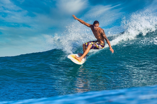 Surfista maschio su un'onda blu al giorno pieno di sole