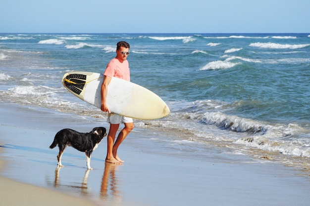 Surfista maschio sulla spiaggia con un cane.