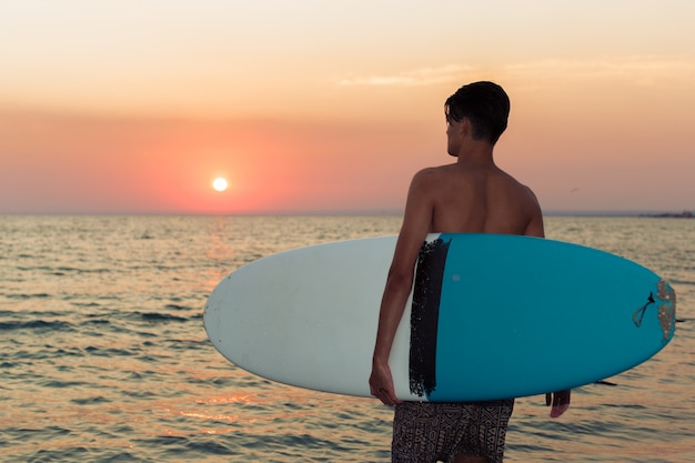 Surfista tenendo la sua tavola da surf e alla ricerca di onde