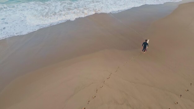 Surfista uomo che lascia impronte camminando sulla spiaggia drone surfista che calpesta la sabbia bagnata