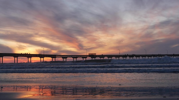 Surfisti che praticano il surfing dalle onde dell'acqua dell'oceano del molo persone e cielo al tramonto in California