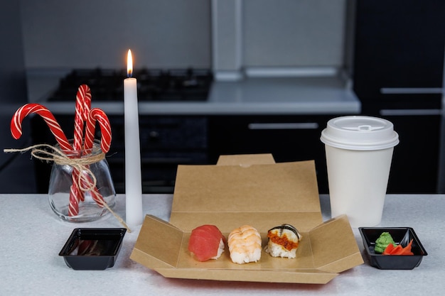 Sushi con gamberi di tonno e anguilla si trova in una scatola di cartone sul tavolo in cucina Concetto natalizio Decorazioni festive sotto forma di figurine di candele e dolci