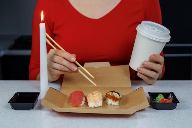 Sushi con gamberi di tonno e anguilla si trova in una scatola di cartone sul tavolo in cucina La ragazza con il maglione rosso mangia con le bacchette Concetto di fast food
