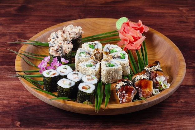 Sushi e panini su un piatto di legno con spezie e foglie verdi. Tavolo di legno. Cibo tradizionale orientale