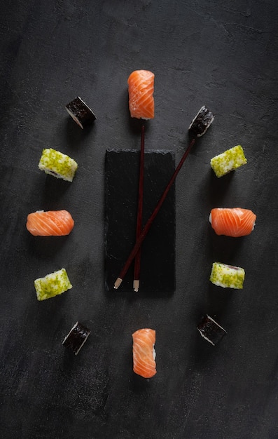 Sushi giapponese in servizio foderato a forma di quadrante con lancette. Vista dall'alto, primo piano su sfondo scuro.