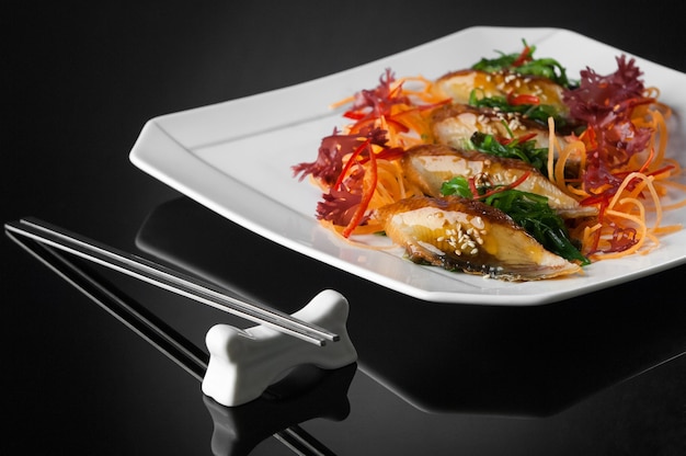 Sushi in un piatto bianco con le bacchette su uno sfondo nero con riflesso