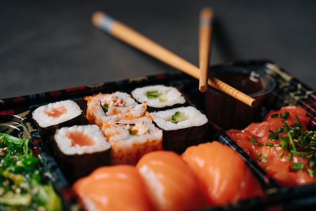 Sushi per andare concetto. Scatola di raccolta con sushi. Con involtini di sushi e bacchette. Maki. Sashimi. Salmone. Tonno. Wasabi. Asiatico. Giapponese.