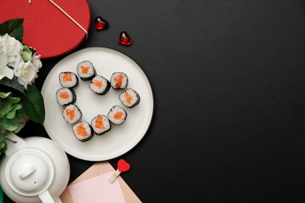 Sushi per San Valentino - rotolare a forma di cuore, sul piatto su sfondo nero. Disteso.