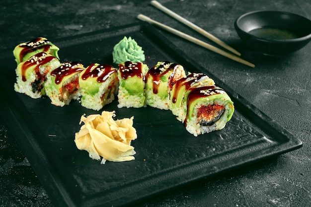 Sushi Roll drago verde con avocado, anguilla e caviale tobiko su un piatto nero su sfondo scuro. Consegna del cibo. cucina giapponese