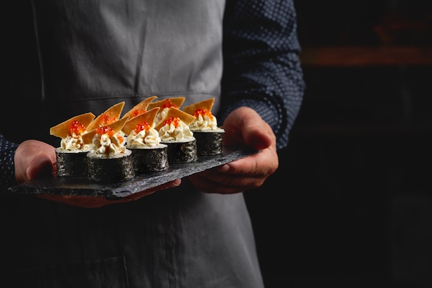 Sushi roll maki futo cibo giapponese su una lastra di pietra nera nelle mani di un cameriere.