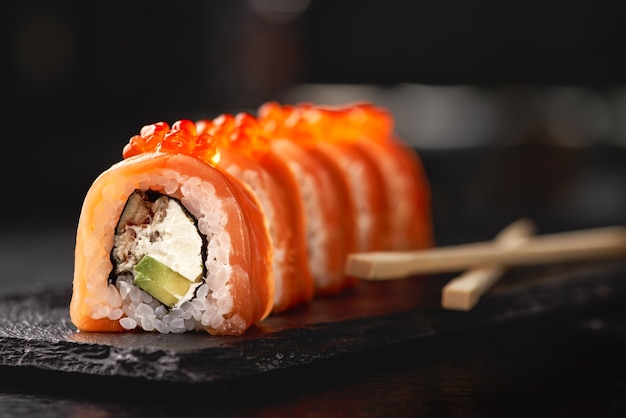 Sushi roll maki futo cibo giapponese su una lastra di pietra nera nelle mani di un cameriere.